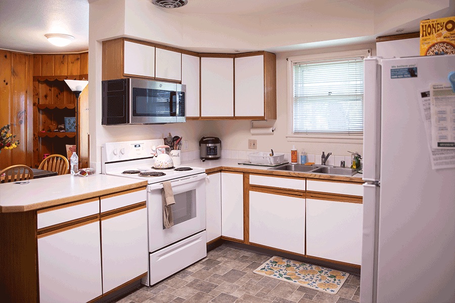A bright kitchen with white cabinets and appliances and a view into the dining room.
